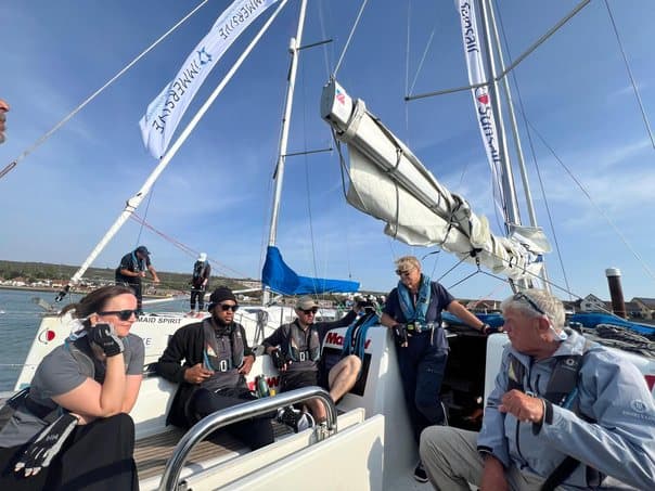 Crew members seated in the cockpit during a briefing, with the boom and rigging overhead.
